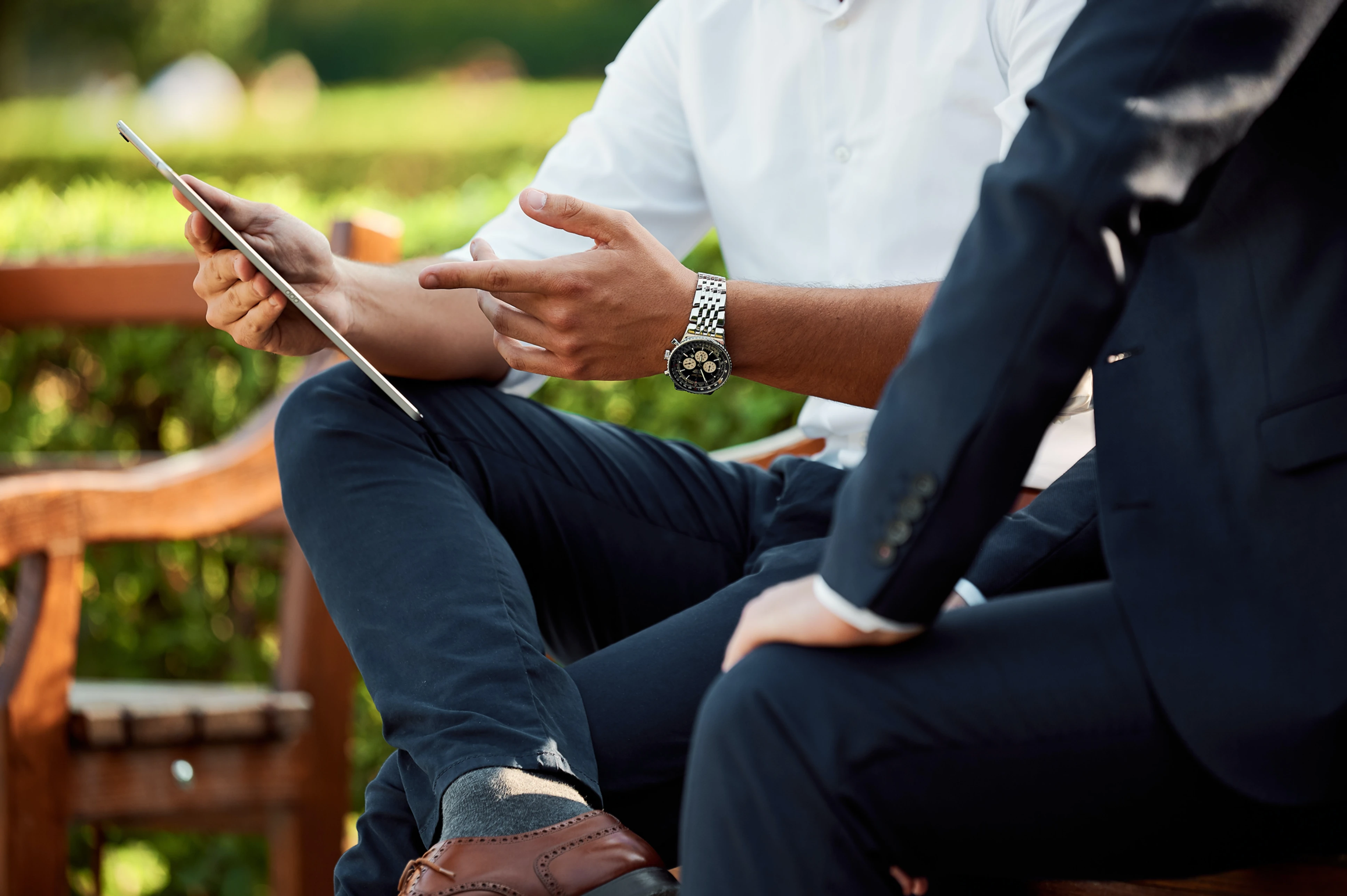 Two business men looking at a tablet while sitting on a park bench